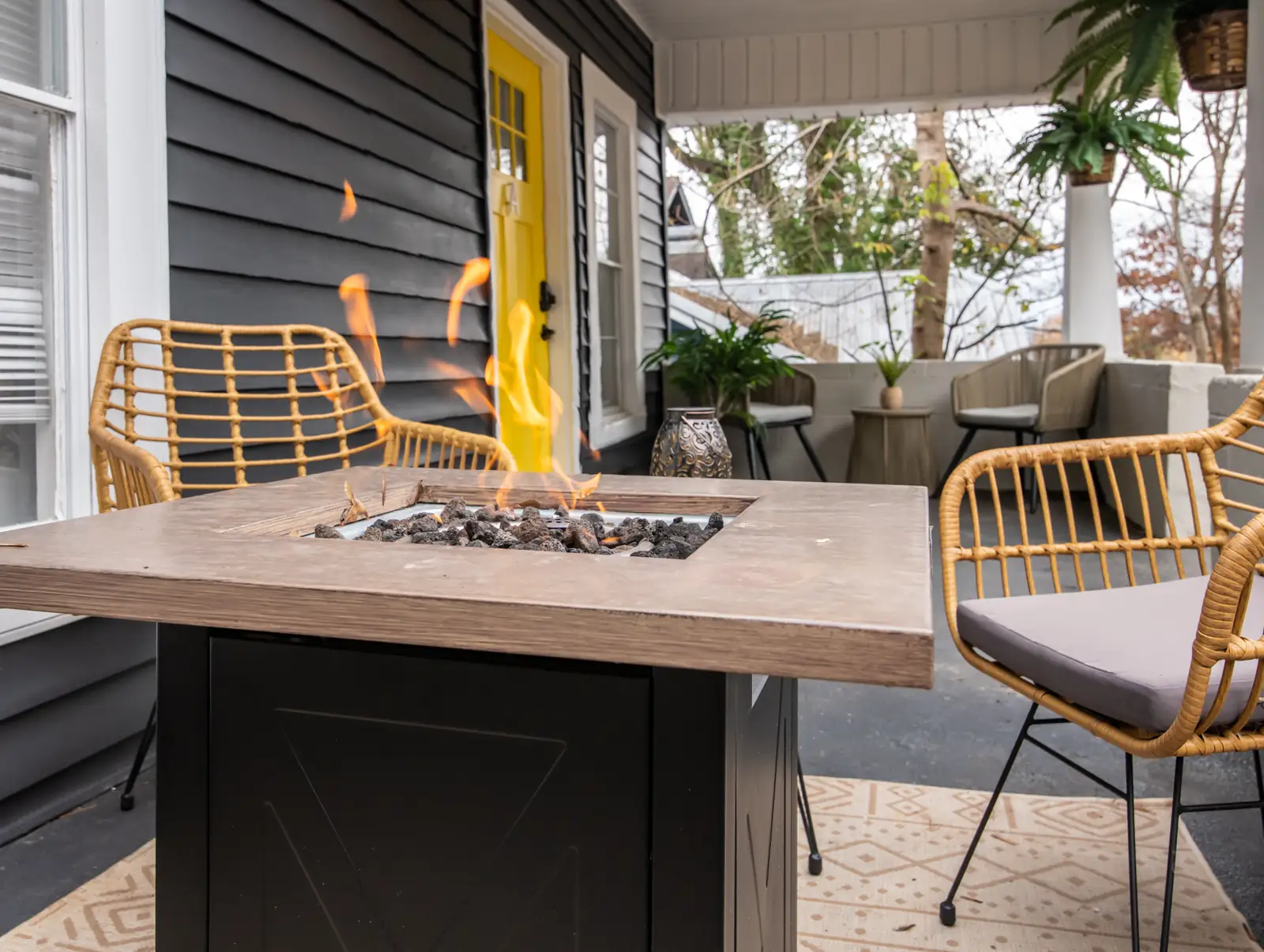 Covered porch with a lit fire table and rattan chairs